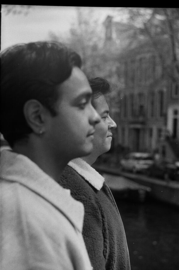 A black-and-white analog portrait of two men gazing along an Amsterdam canal during their LGBT engagement photography session in Amsterdam