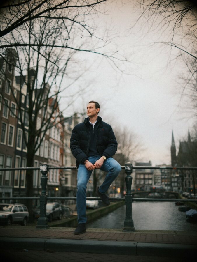 A stylish man in a dark sweater standing on a bridge, reflecting the authentic look needed for dating in Amsterdam as an expat