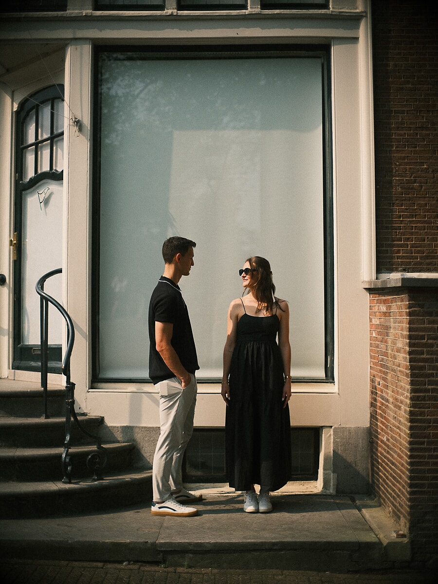 Engagement SP4 Elegant engagement portrait of a couple in black outfits beside a tall window of an Amsterdam canal house