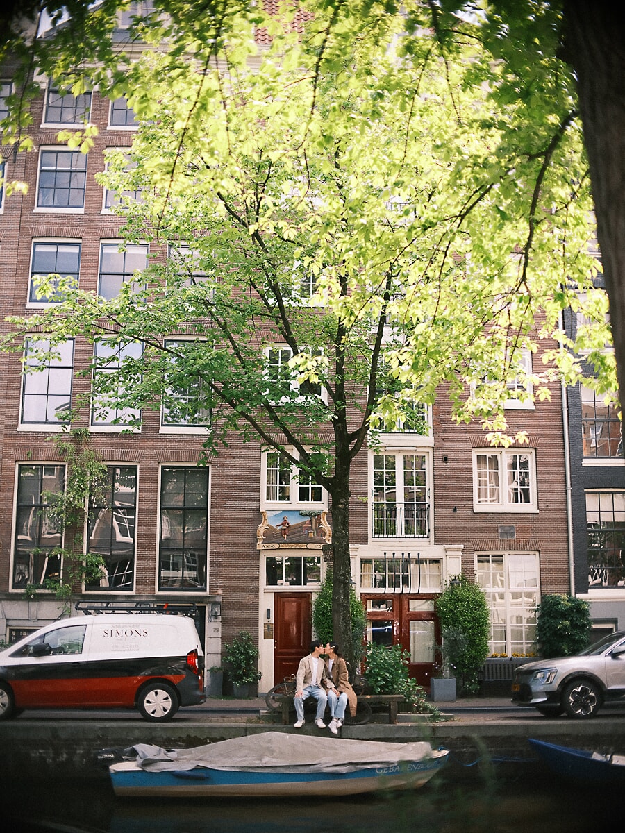 Loveshoot SP11 Documentary couple portrait of partners kissing on a bench beneath a tall Amsterdam canal house