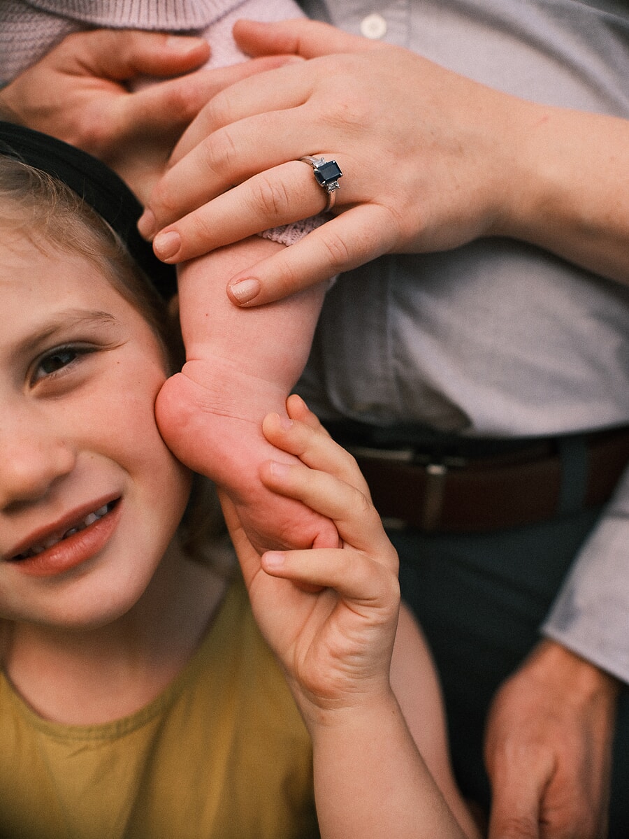 Family SP11 Candid close-up of a baby's foot resting against a smiling sibling's cheek, a sweet detail from a family photo session
