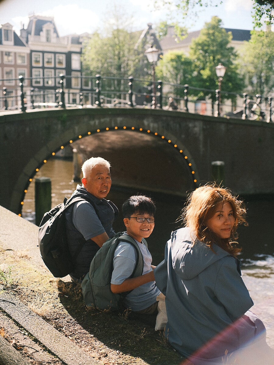 Family SP13 Three generations crouching beside a canal beneath an arched bridge strung with lights, captured by a family photographer in Amsterdam