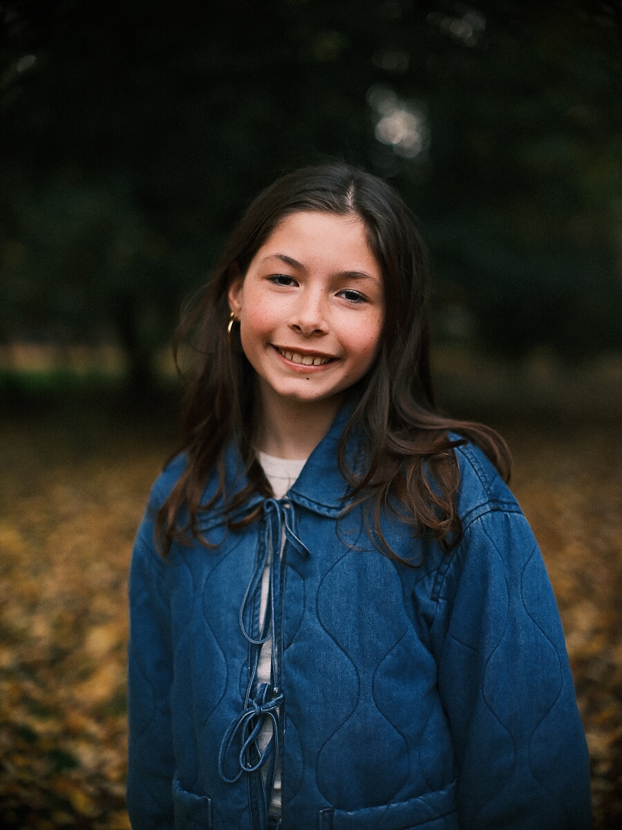 Family SP15 Relaxed children's portrait of a smiling girl in a denim jacket among autumn leaves in an Amsterdam park