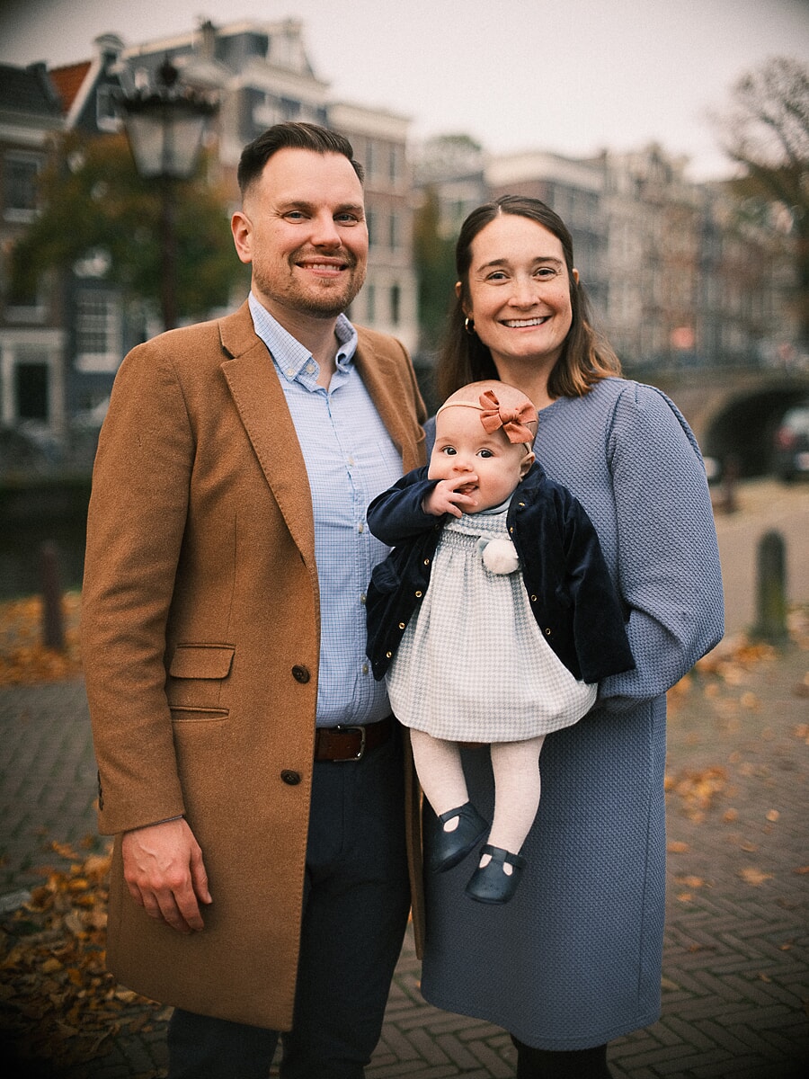 Family SP16 New parents cradling their baby on a canal bridge in autumn, a portrait by a family photographer in Amsterdam, the father in a camel coat