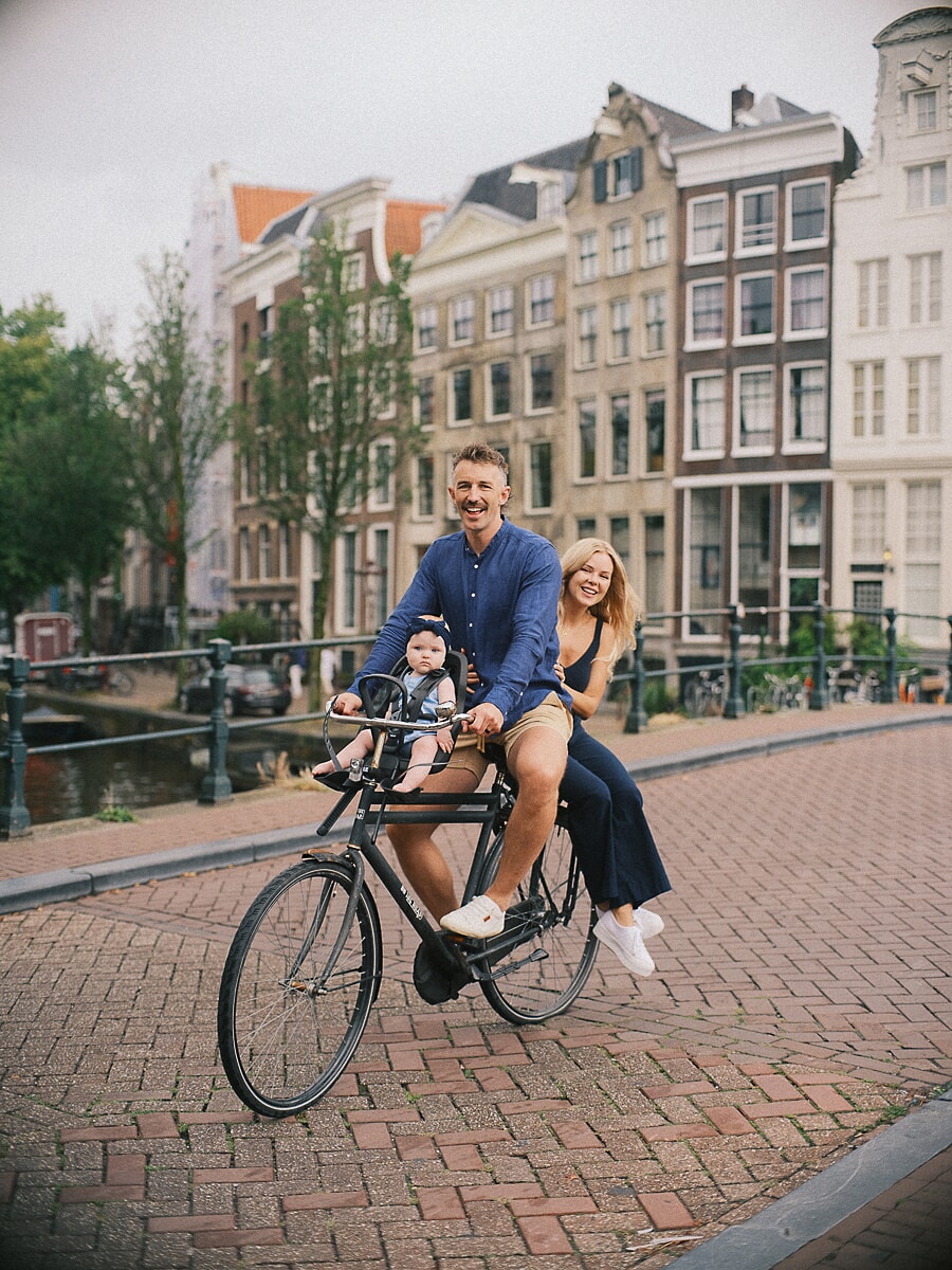 Family SP2 Joyful family photoshoot as parents cycle along an Amsterdam canal with their baby in a bike seat in summer