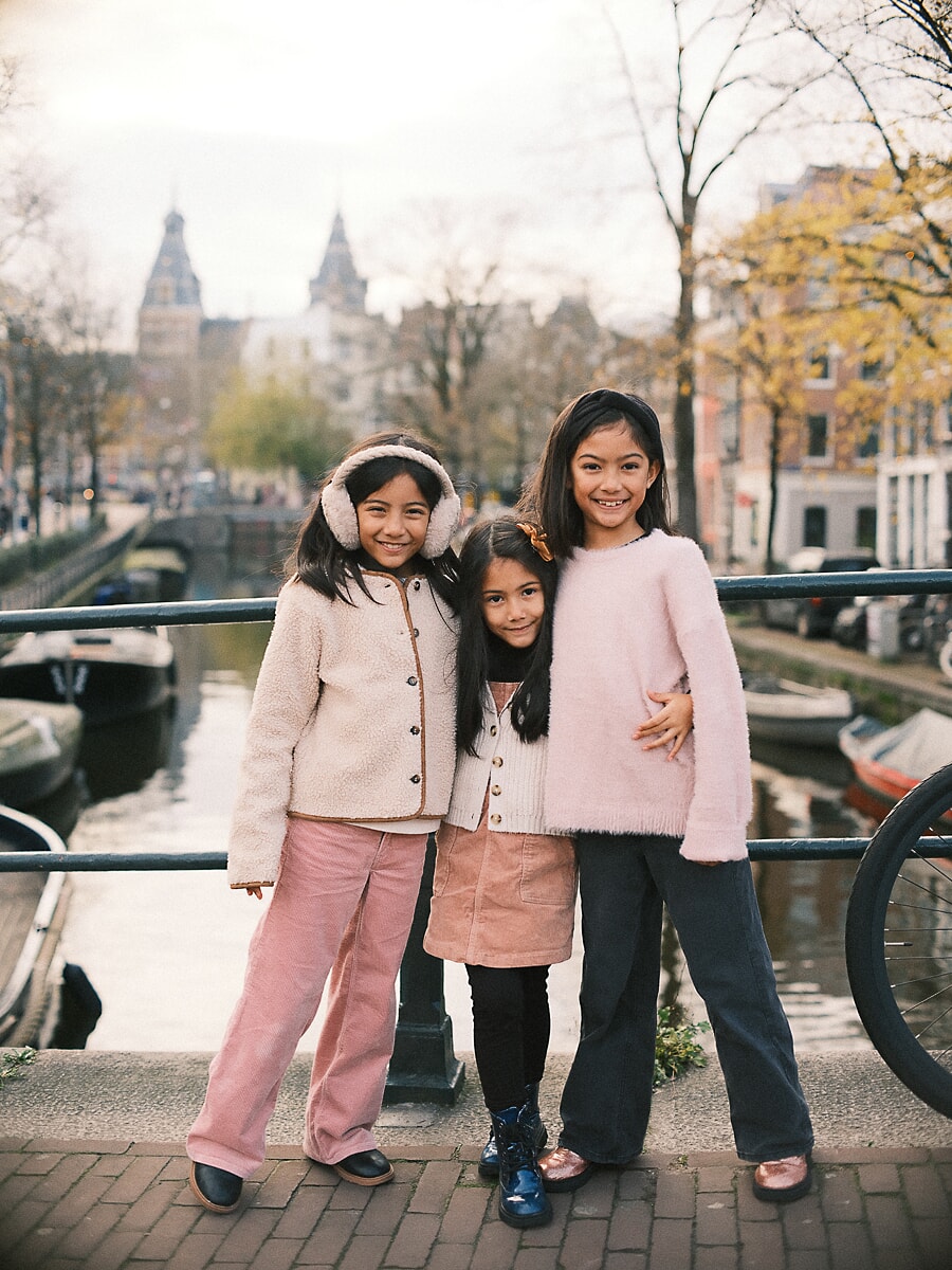Family SP4 Sisters in pink and cream posing by an Amsterdam canal railing, a cheerful frame from a children's photoshoot