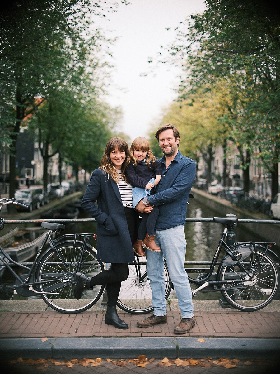 Family SP8 Family photographer in Amsterdam captures parents with their toddler beside canal bicycles on an autumn afternoon