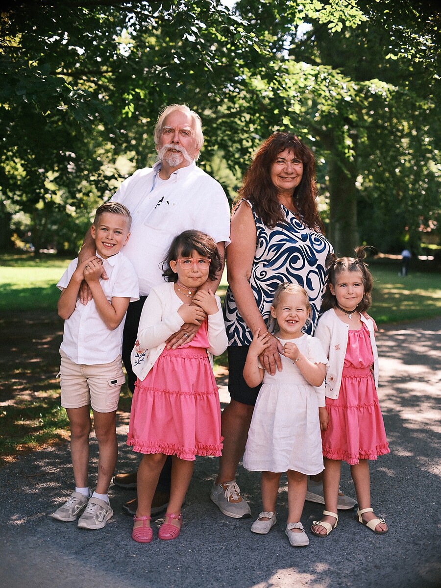 Group Family SP10 Family photographer in Amsterdam captures grandparents with their four grandchildren in a sunlit park, the children in pink and white
