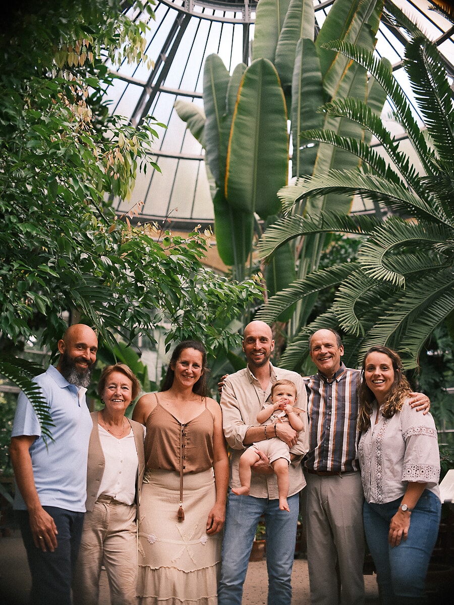 Group Family SP4 Expat family of three generations surrounded by tropical greenery inside a botanical glasshouse, a baby held at the centre during their family photography session