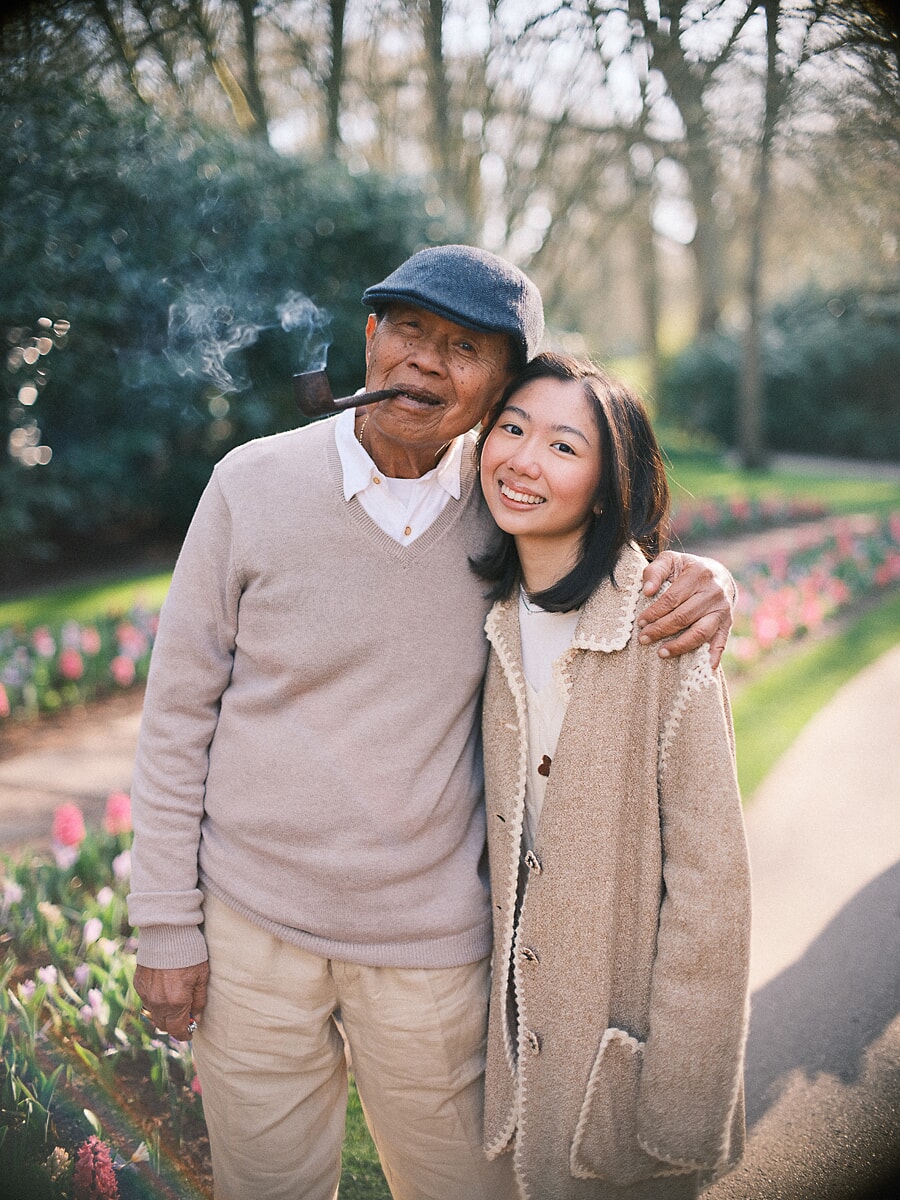 Group Family SP5 Grandfather in a flat cap smoking a pipe beside his smiling granddaughter among spring tulips, a tender frame from a day of family photography