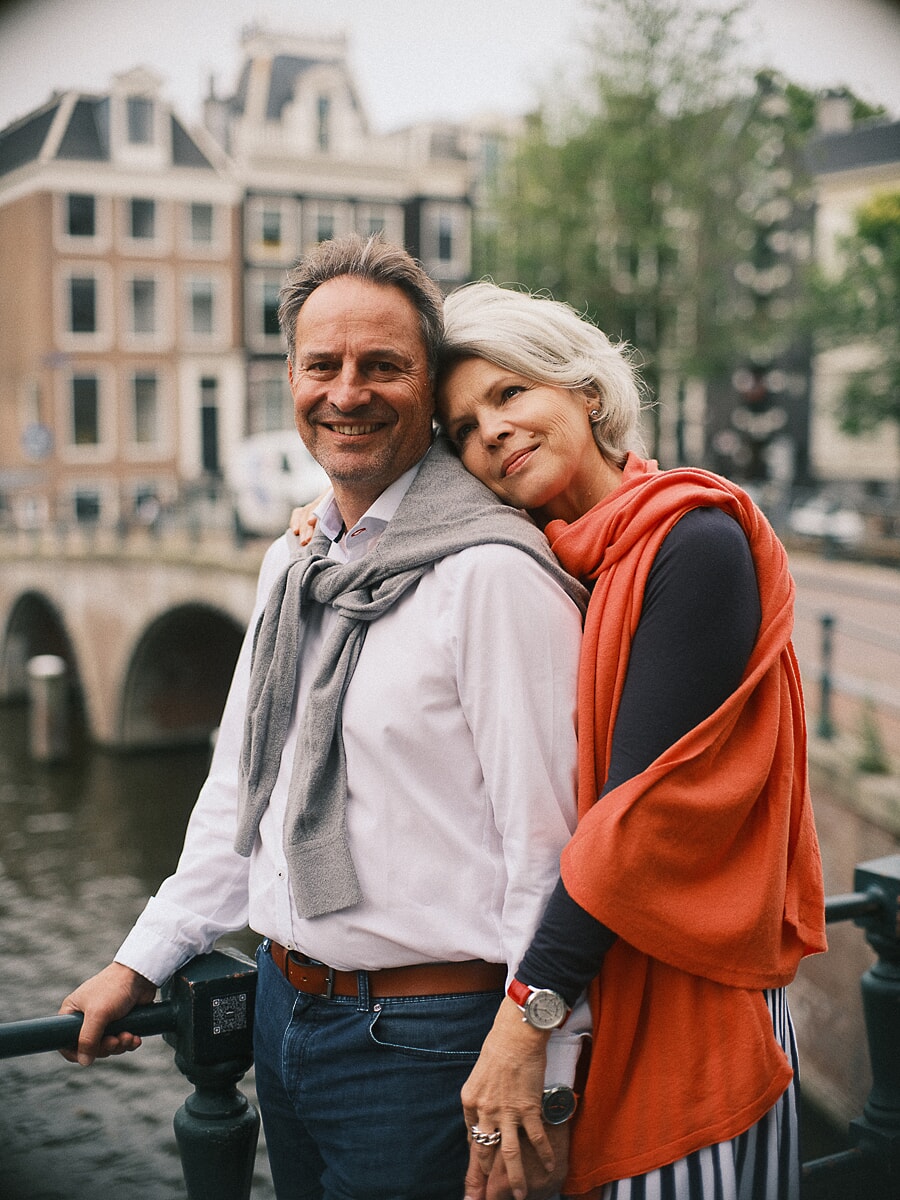Group Family SP7 Golden anniversary portraits of a couple embracing beside an Amsterdam canal, the woman in an orange wrap resting her head on her partner's shoulder