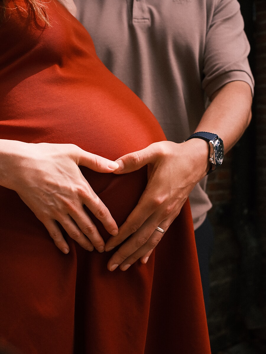 Maternity SP5 Intimate maternity photographs of a couple forming a heart with their hands over the baby bump, the mother-to-be in a rust-coloured dress