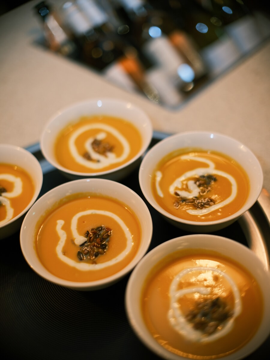 Five bowls of pumpkin soup with a swirl of cream and toasted seeds, ready on a tray