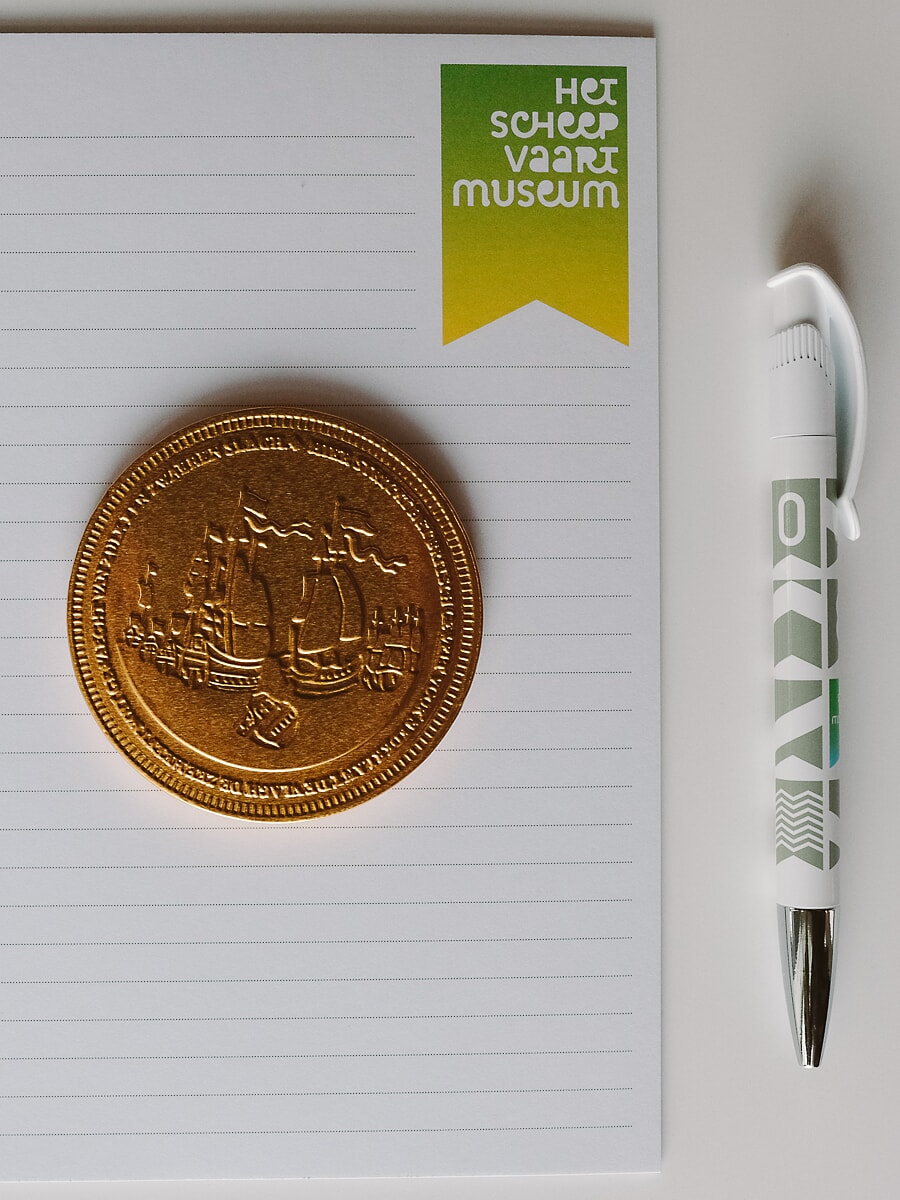 Flat-lay of a lined notepad, an embossed gold medal and a branded pen, merchandise photography for an Amsterdam business