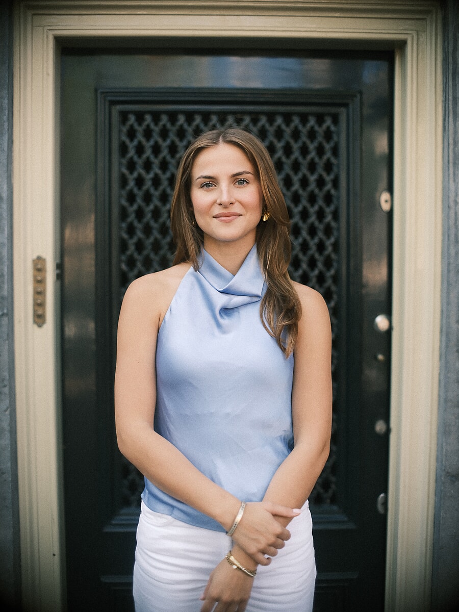 Woman in a pale blue halter top standing in the dark panelled doorway of a canal house, a business portrait in Amsterdam