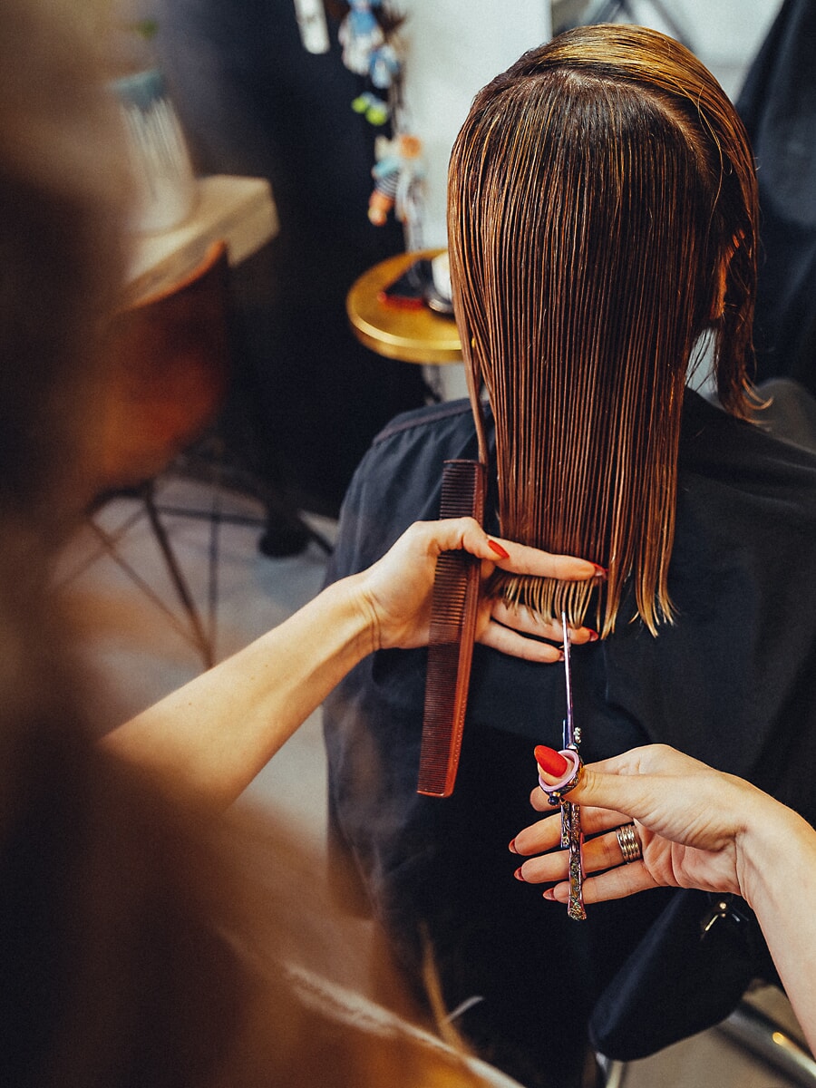 Close-up of two hands cutting a length of wet hair with comb and scissors