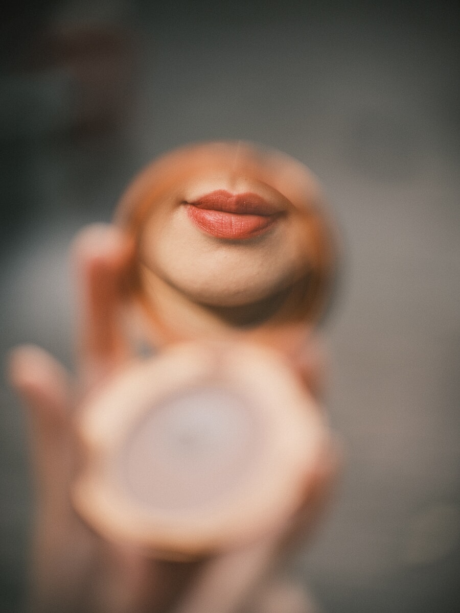 Extreme close-up of a hand holding a round compact mirror that reflects a woman's lips, everything else falling soft