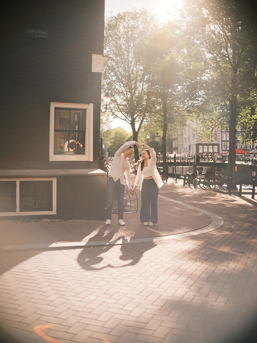 Couple in white shirts turning under their joined hands on a brick street corner in Amsterdam, low sun and long shadows