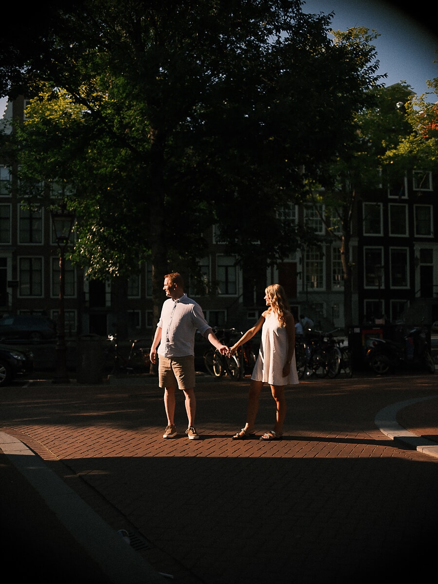 Couple holding hands at arm's length in a shaft of evening light, an in-the-moment shot on an Amsterdam street