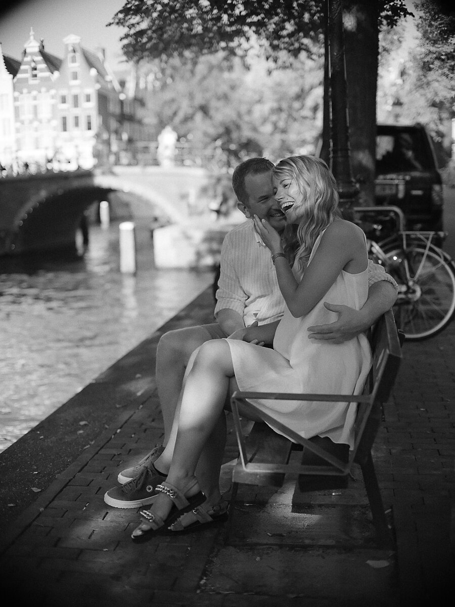 Couple laughing on a canal-side bench in Amsterdam, a black-and-white frame from their photo session