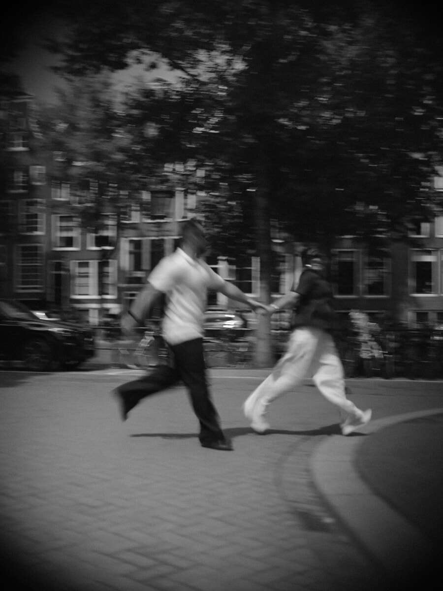 Black-and-white motion blur of a couple running hand in hand through the city, unstaged and in the moment