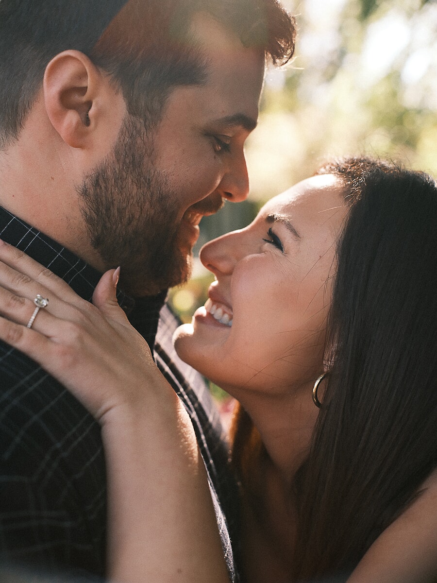Laughing face to face in an Amsterdam park, her engagement ring against his neck during their couple session