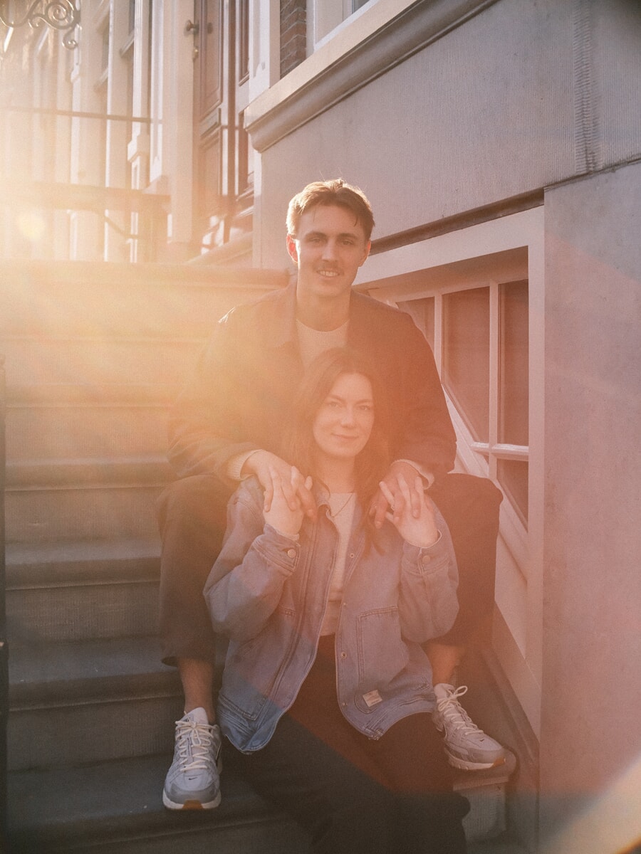 Engaged couple on stone steps in golden hour light during their engagement photoshoot in Amsterdam