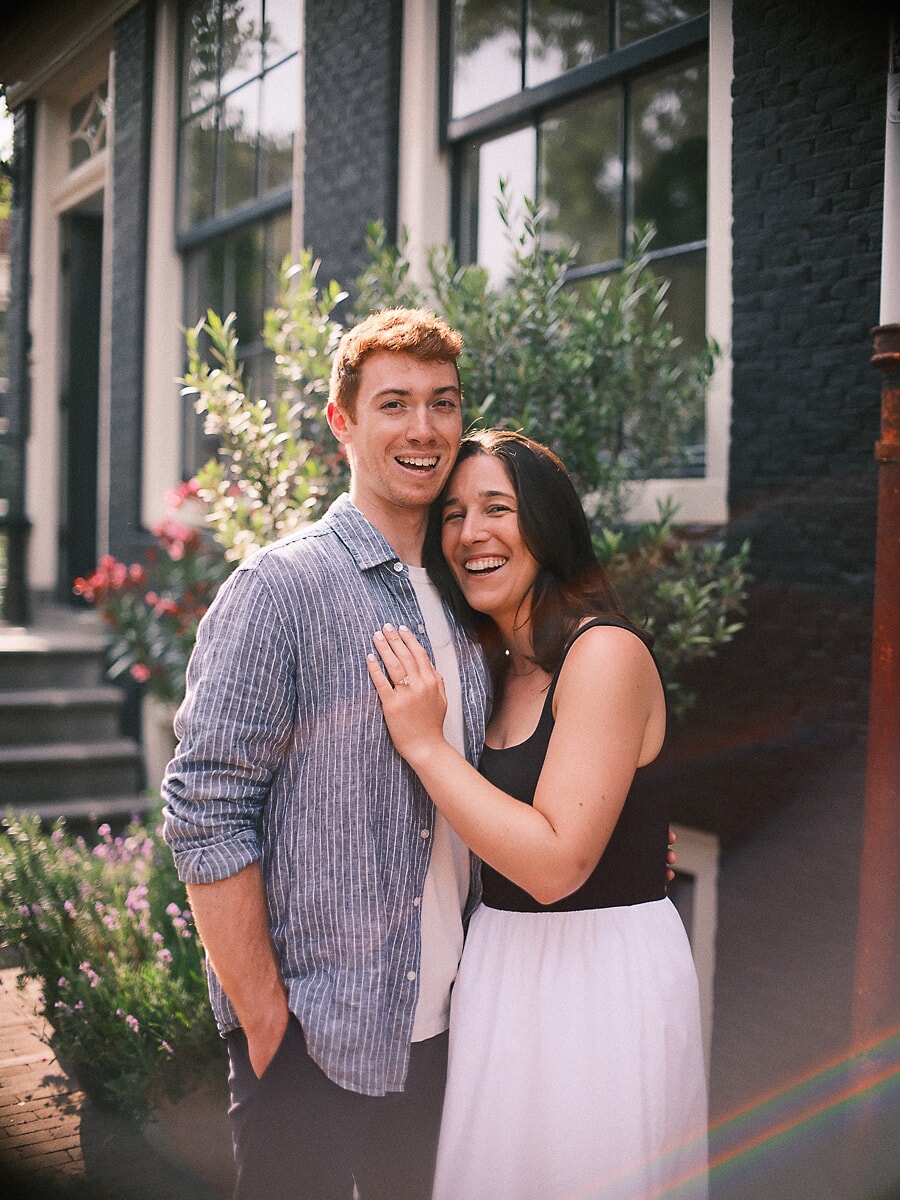 Engaged couple laughing outside a dark Amsterdam canal house, her hand with the ring on his chest