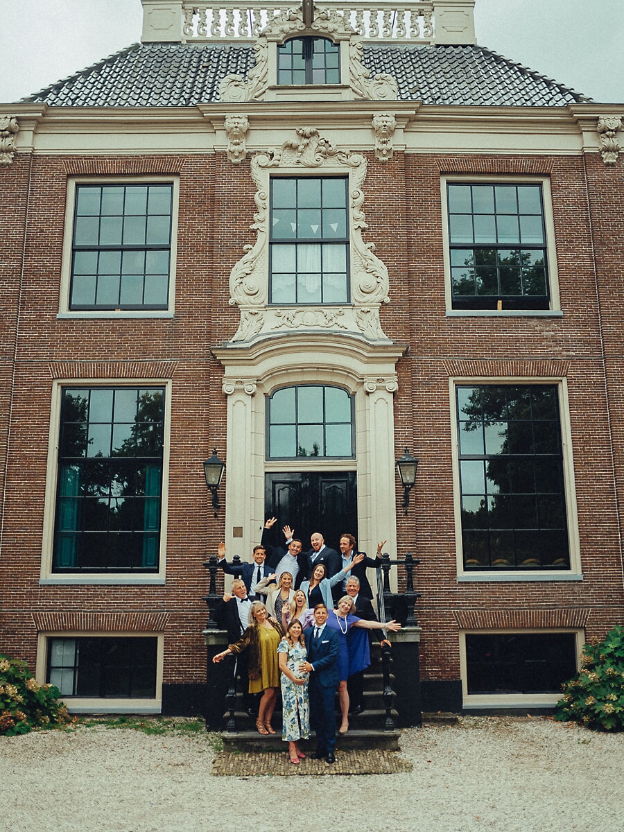 Group Family SP14 Extended family waving from the steps of a grand Dutch country house, an exuberant multigenerational photo session in front of the ornate brick facade
