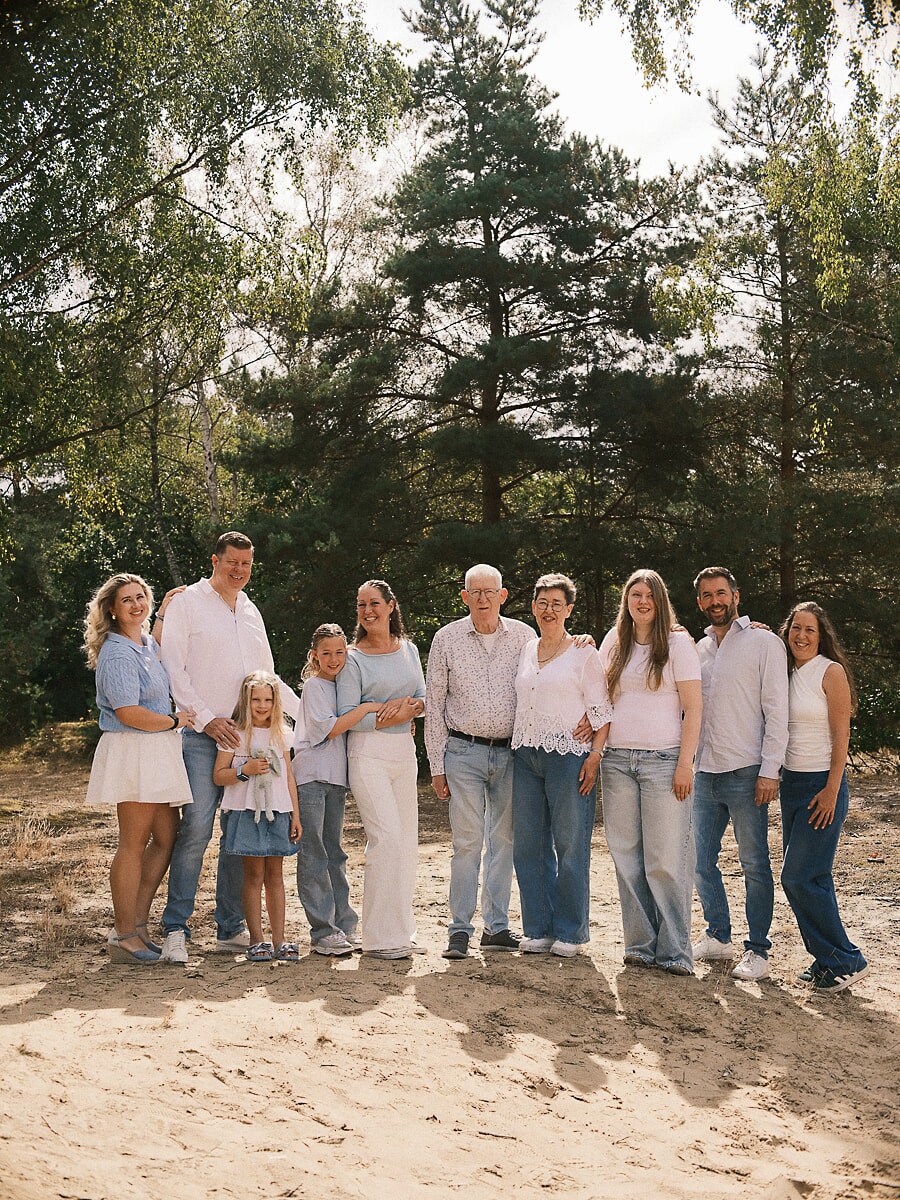 Ten family members in blue and white standing together on sand in a Dutch woodland, the grandparents at the centre
