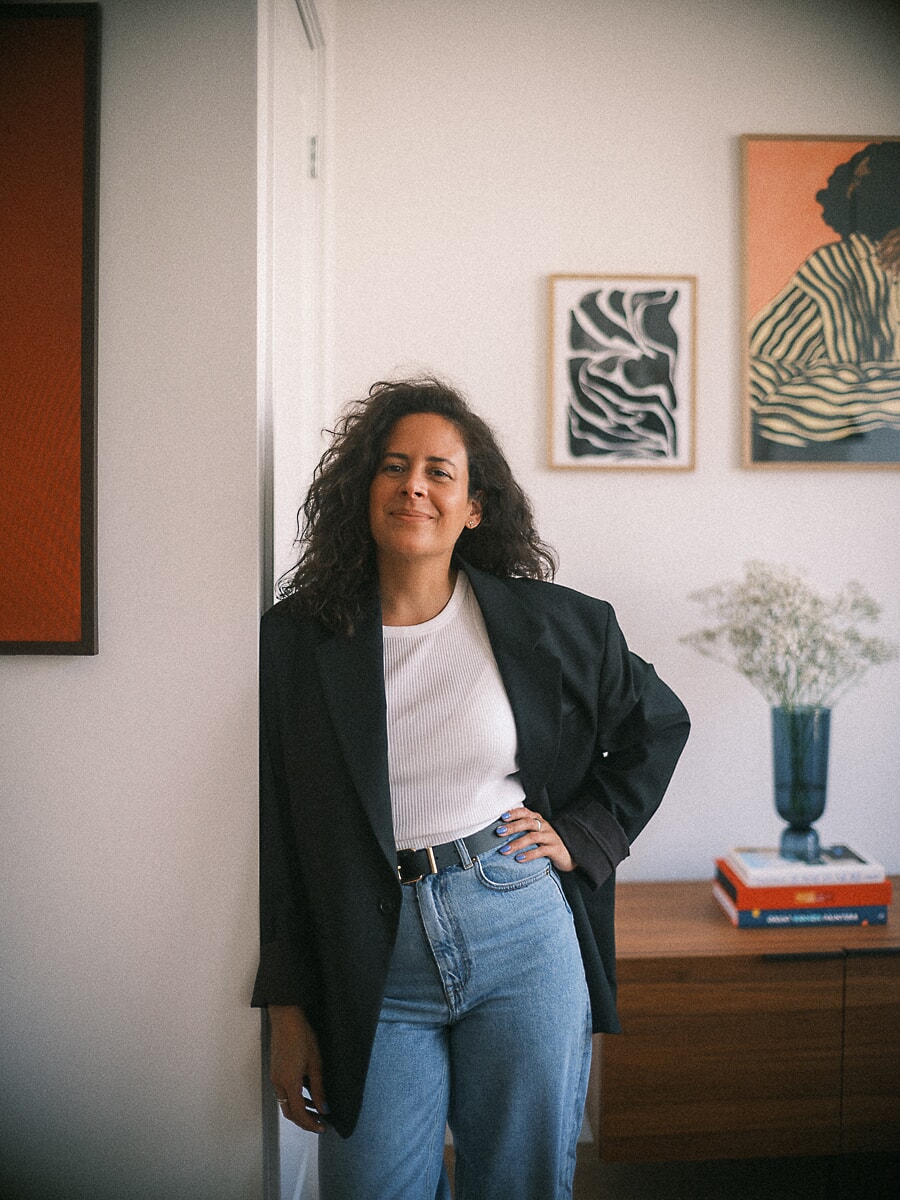 Founder in an oversized blazer leaning in a doorway, framed prints and a walnut sideboard behind her, a branding portrait in Amsterdam
