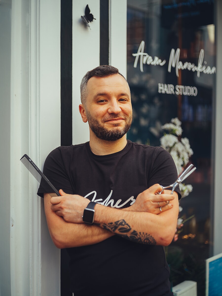 Hairdresser with a comb and scissors folded across his chest, standing at the window of a salon