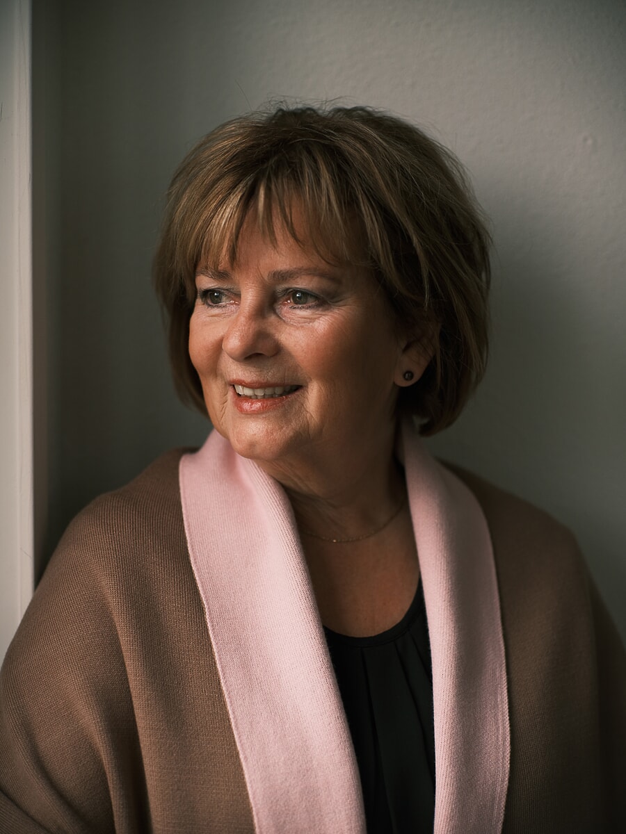 Woman in a camel wrap with pink trim looking off into soft window light, a corporate headshot in Amsterdam