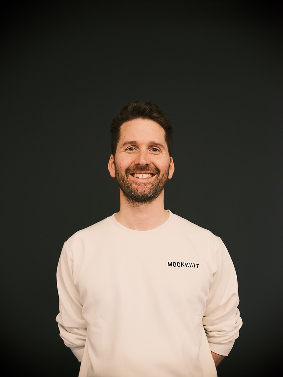 Man in a cream sweatshirt laughing against a plain dark grey backdrop, a business headshot in Amsterdam