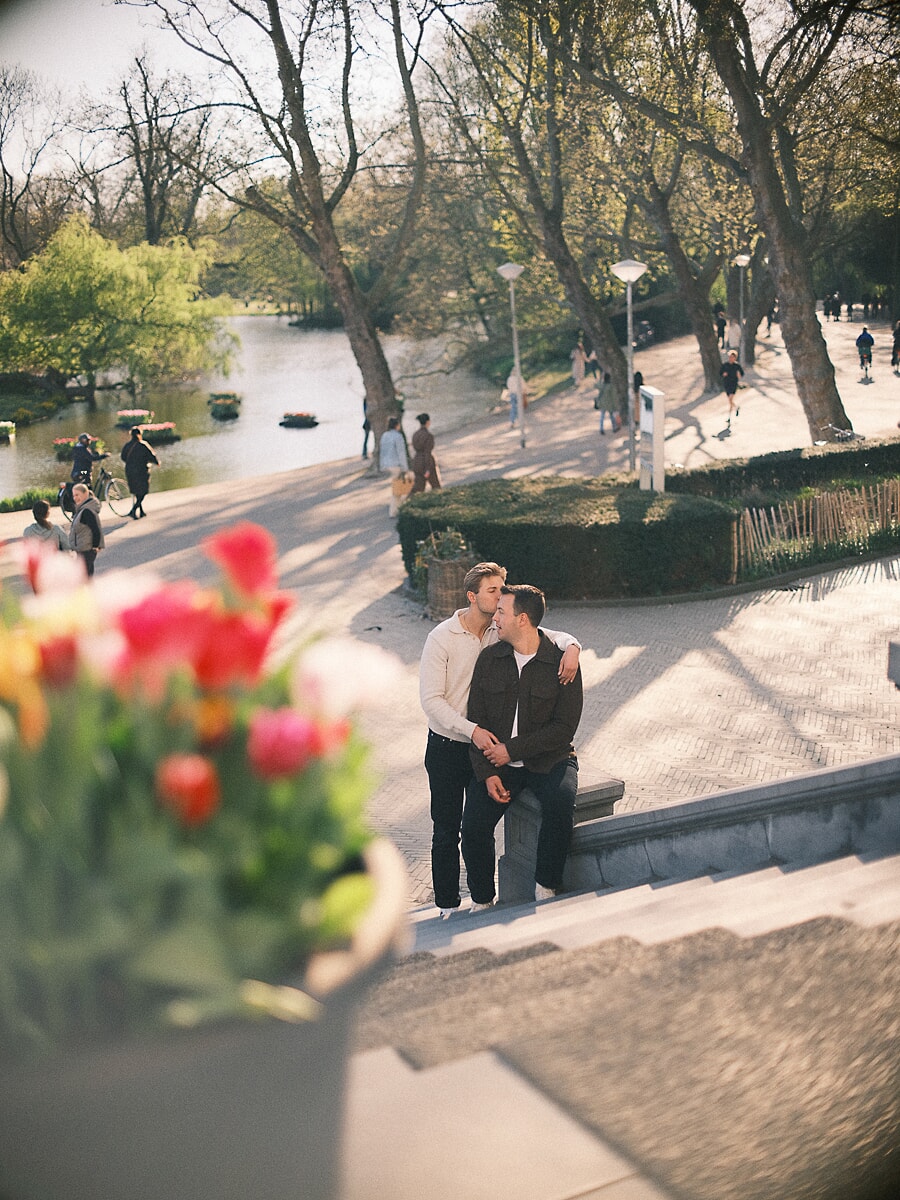 Two men sharing a kiss on the steps at Vondel CS in Amsterdam's Vondelpark, a loveshoot among the tulips