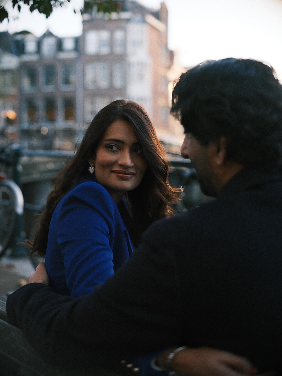 Woman glancing back over her partner's shoulder at dusk beside an Amsterdam canal