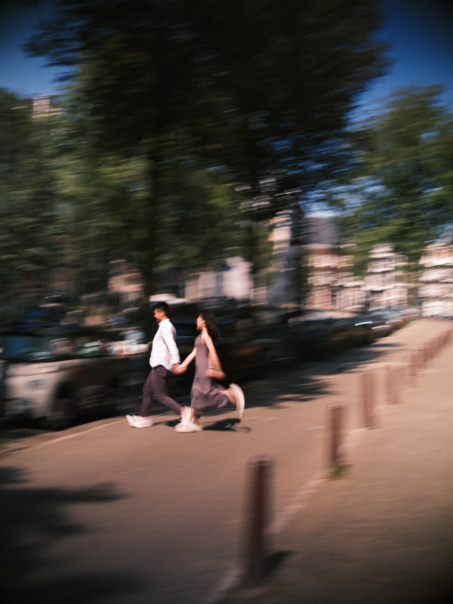Couple running hand in hand along a canal street in motion blur during their loveshoot in Amsterdam