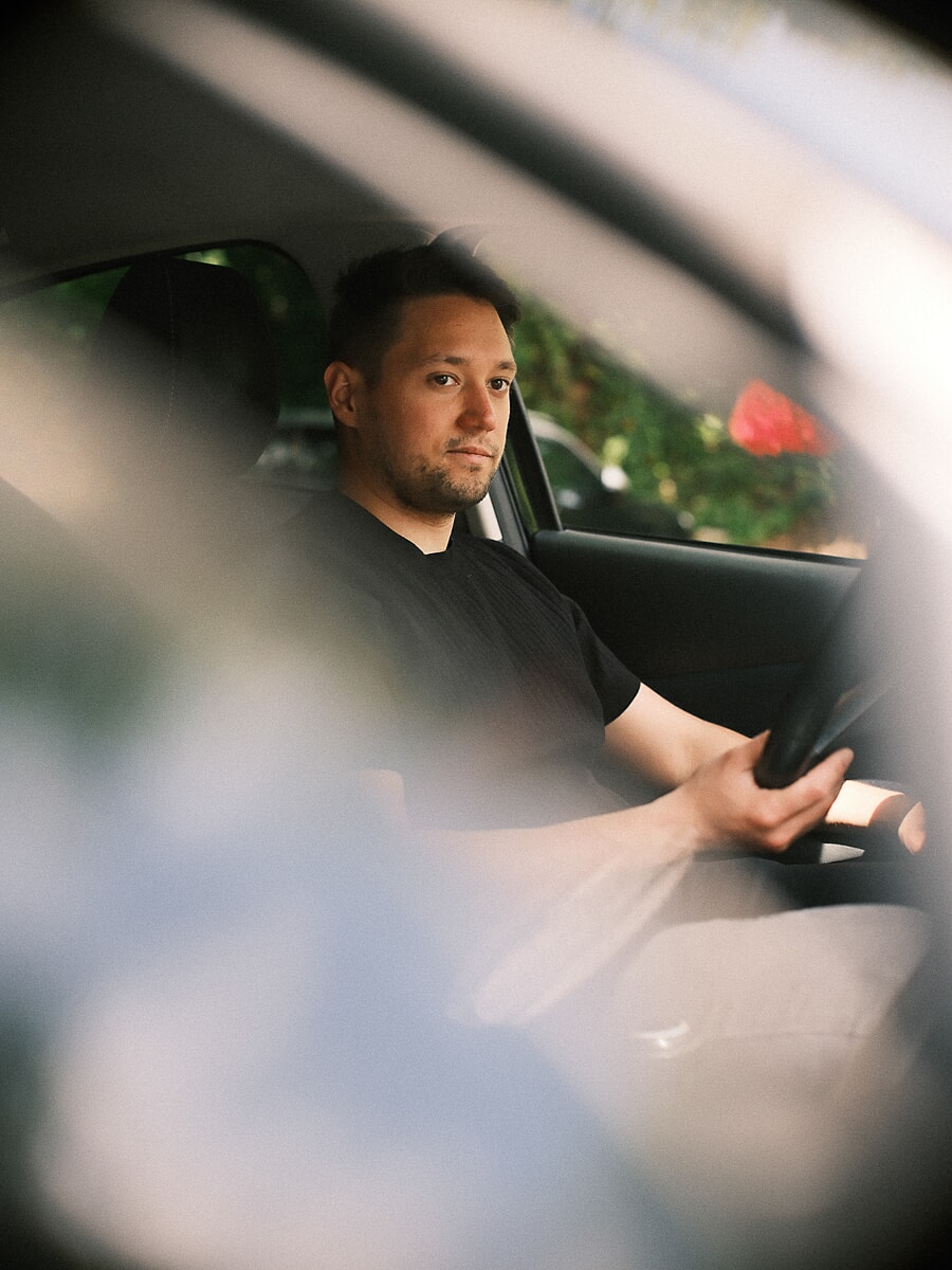Man at the wheel of a car seen through the window frame, the foreground falling away into blur