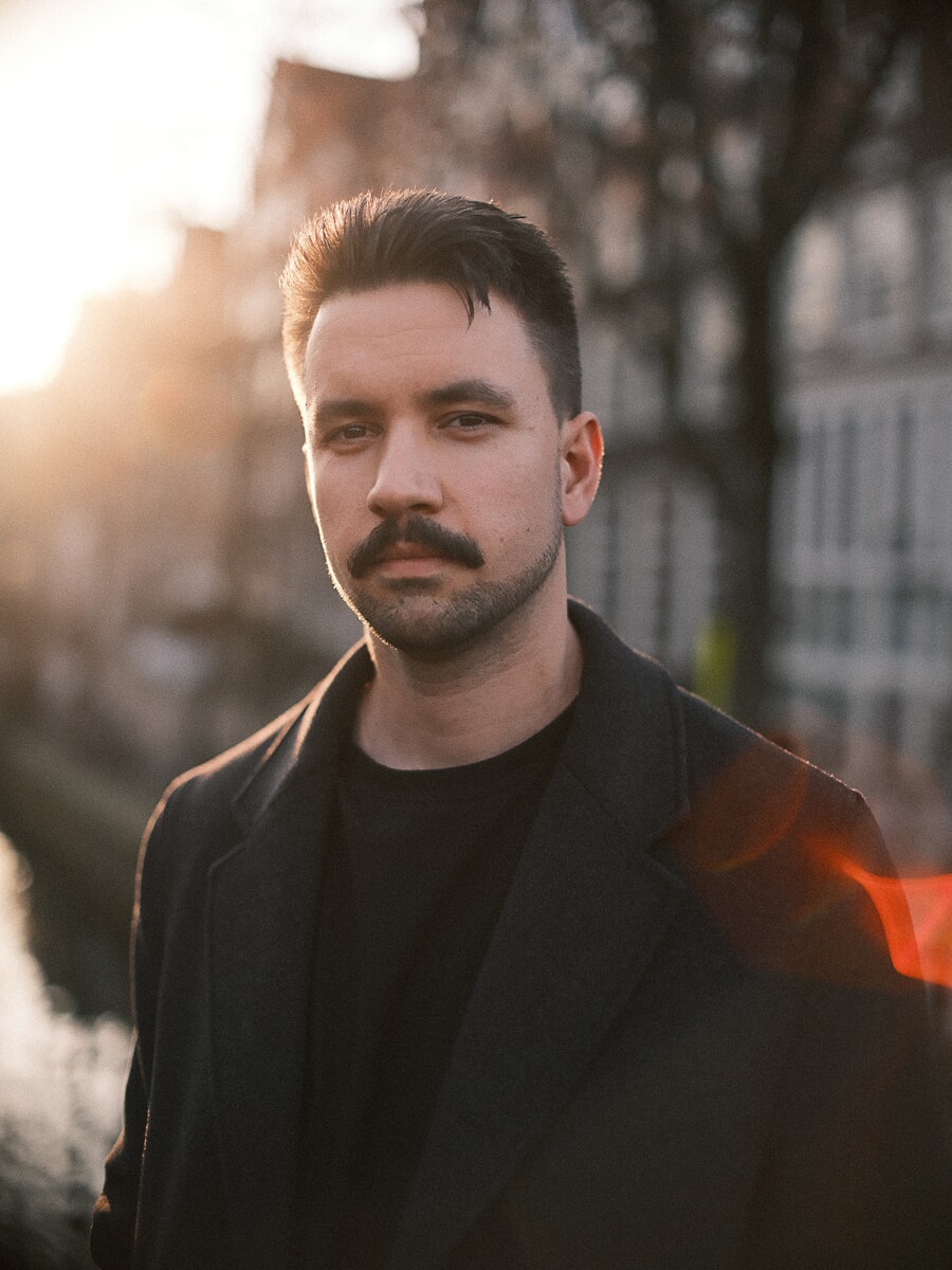 Close portrait of a man in a black coat with the orange halo and flare of an artistic lens across the frame