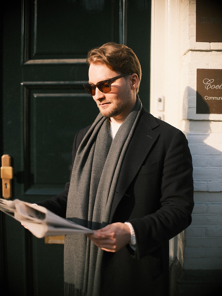 Man in sunglasses reading a newspaper against a dark green door in low winter sun, a spontaneous dating portrait in Amsterdam