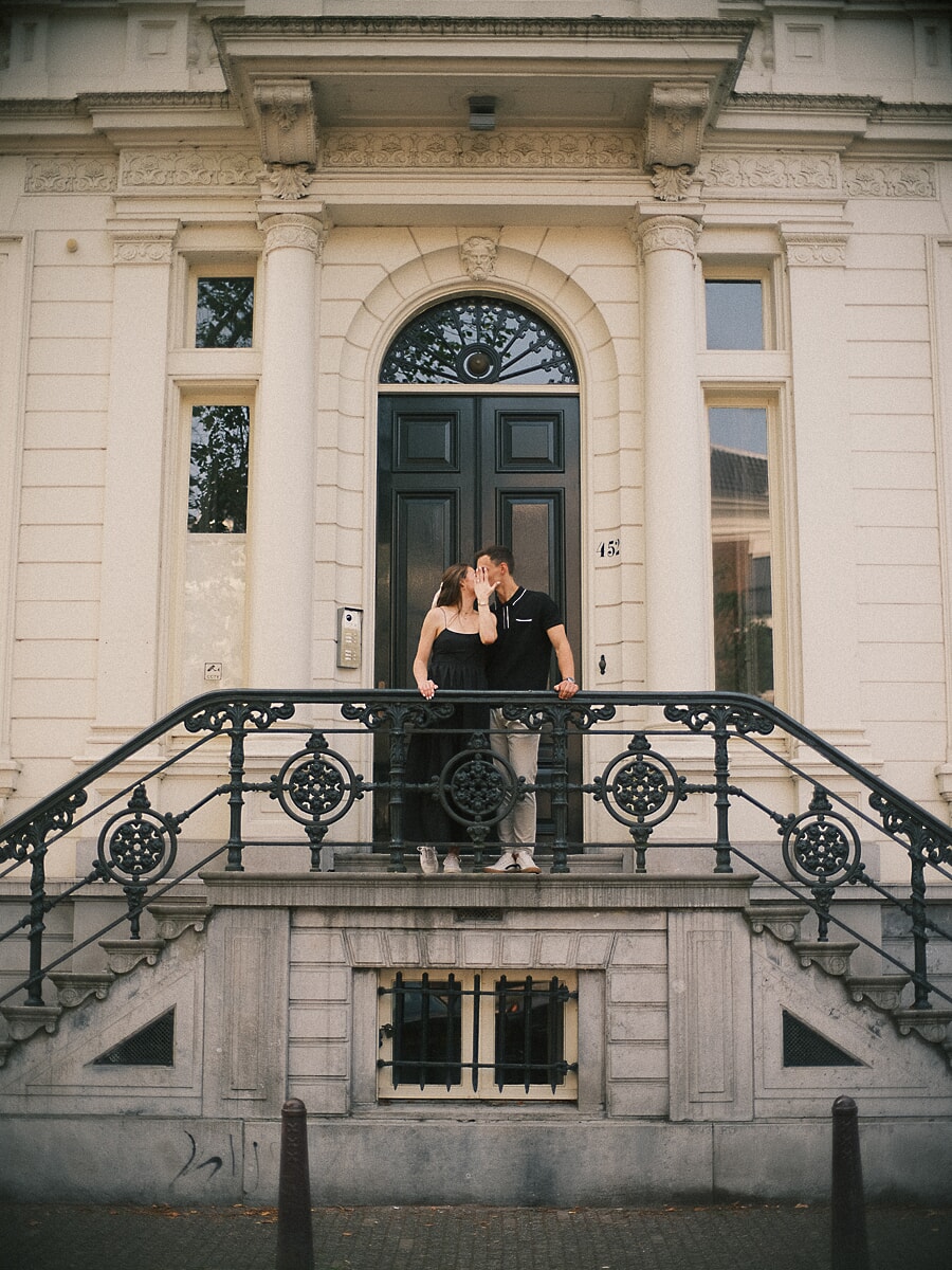 Newly engaged couple kissing on the ornate steps of an Amsterdam canal house in soft afternoon light