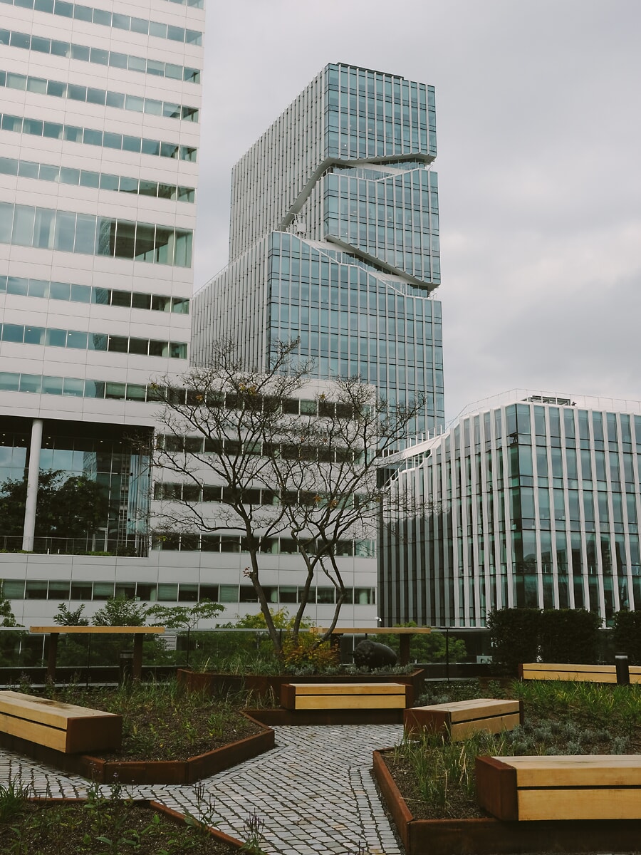 Stacked glass-and-steel office tower above a roof terrace of timber benches, commercial property photography in Amsterdam