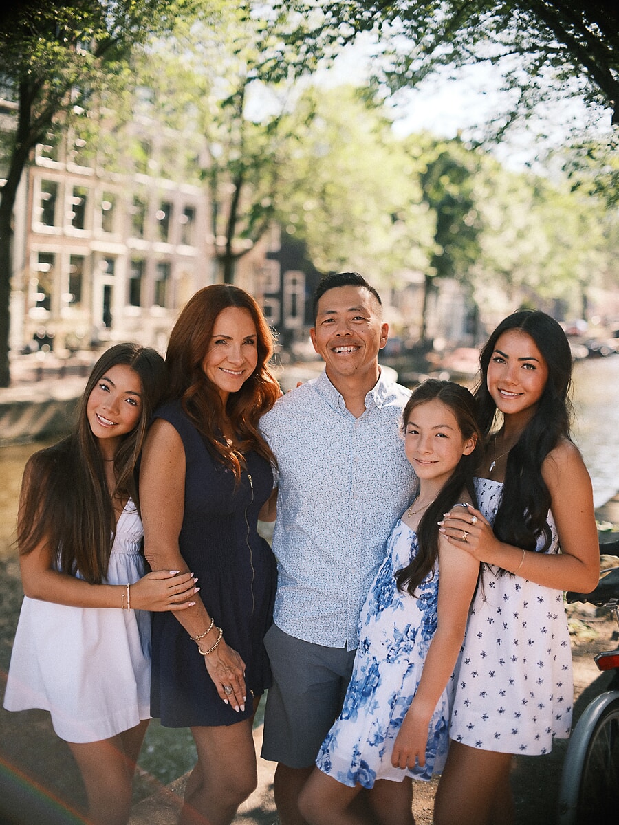 Parents and their three daughters close together beside a sunlit Amsterdam canal in summer