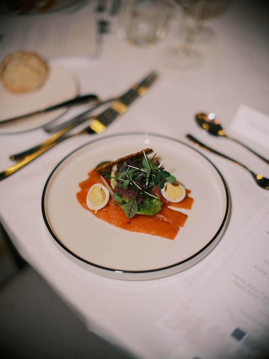 Plated starter of smoked salmon with quail eggs and micro herbs beside gold cutlery and a menu card