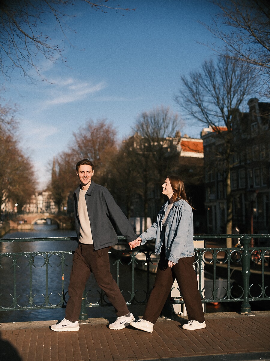 Couple hand in hand across an Amsterdam canal bridge on a clear winter day, a pre-wedding portrait