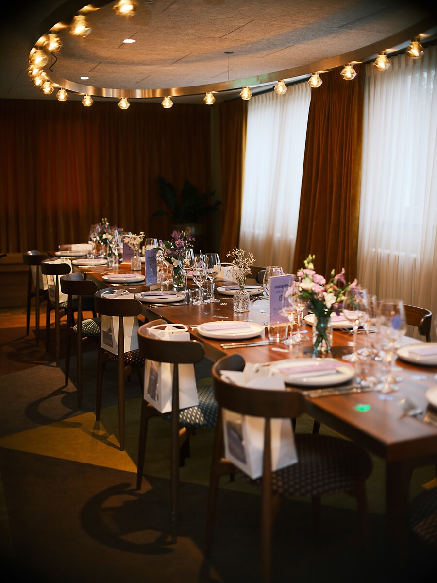 Long table set for a private dinner under a ring of bare bulbs, menu cards and gift bags at every place, a business event in Amsterdam