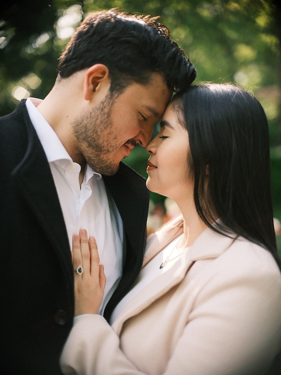 Newly engaged couple forehead to forehead in a park, her engagement ring resting on his chest