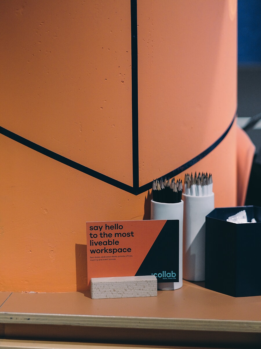 Reception ledge detail: a small printed card between pots of pencils against an orange geometric wall