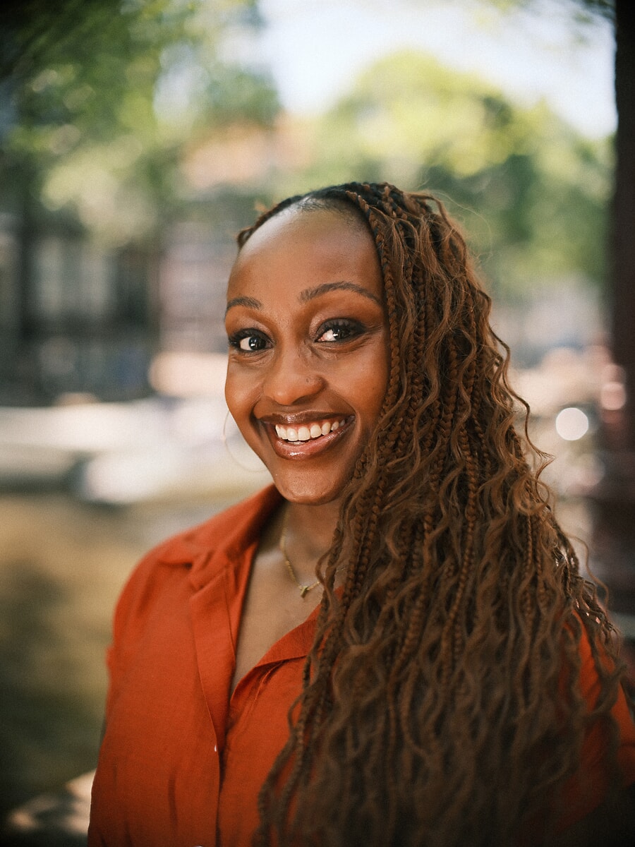 Close smiling portrait of a woman with long braids in a rust shirt against soft green bokeh