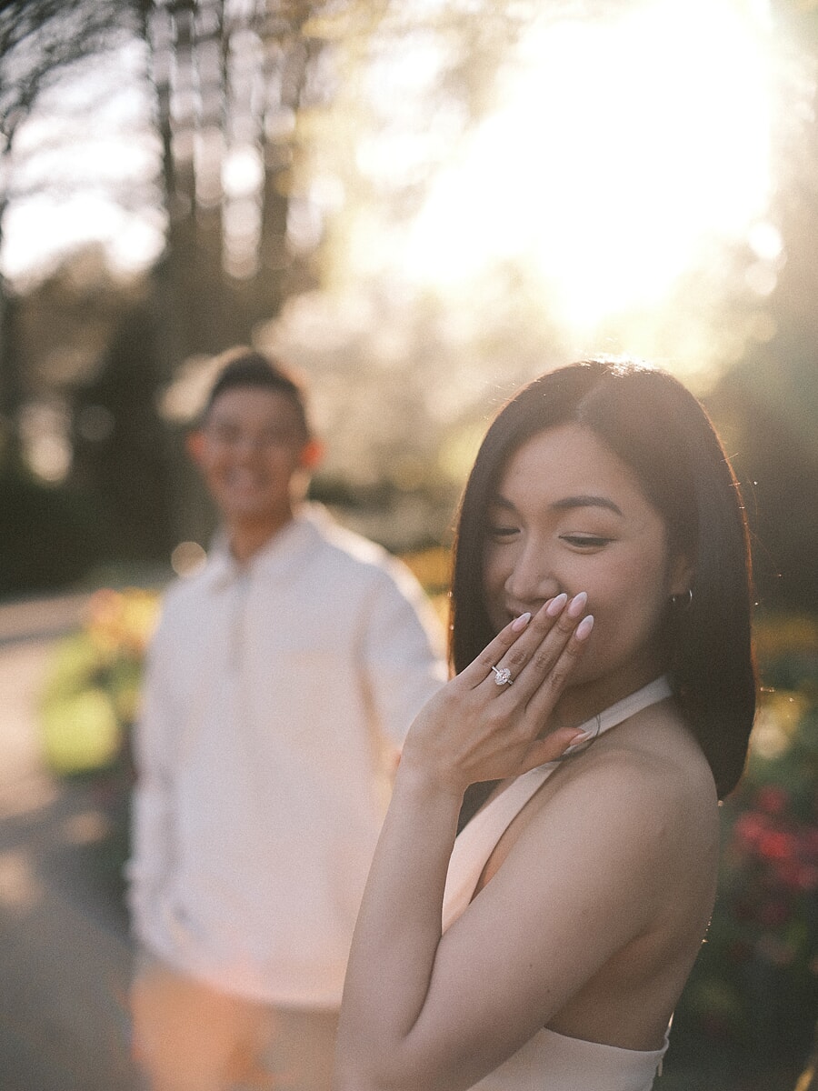 Woman with her hand over her mouth in the first seconds after saying yes, her new engagement ring lit by low sun in an Amsterdam park